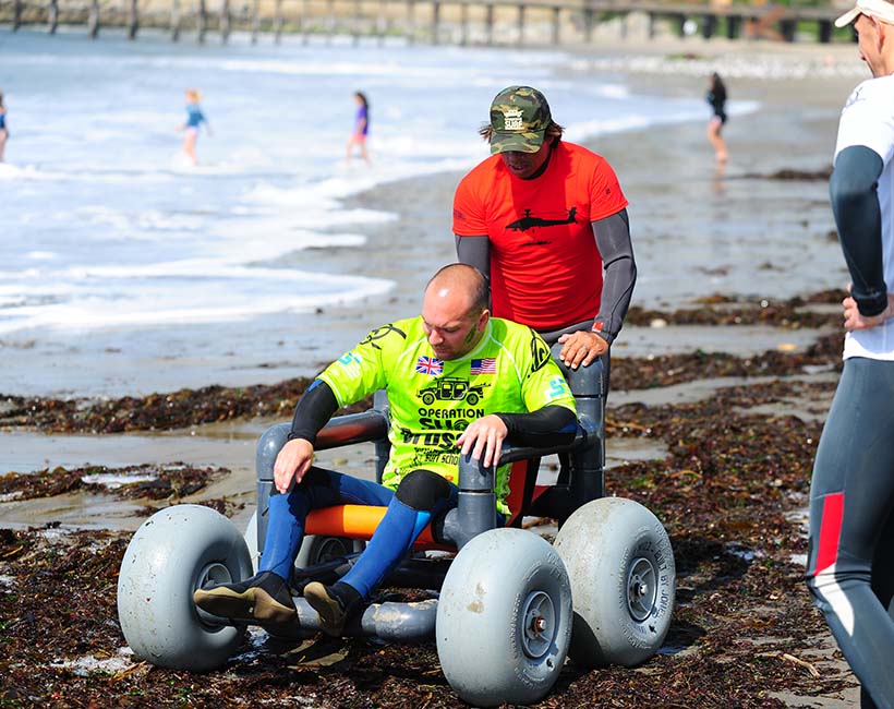 Volunteer assisting disabled surfer in beach wheelchair