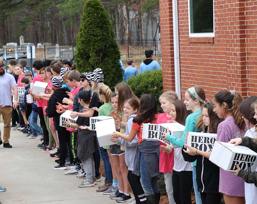 Children in assembly line moving Hero Boxes to be donated