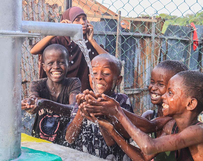a group of children drink from a water spigot with big smiles on their faces